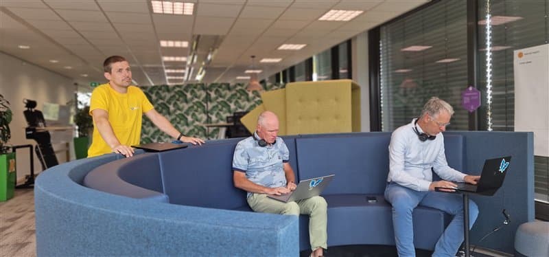 Modern office with three people working on laptops in a circular blue seating area.